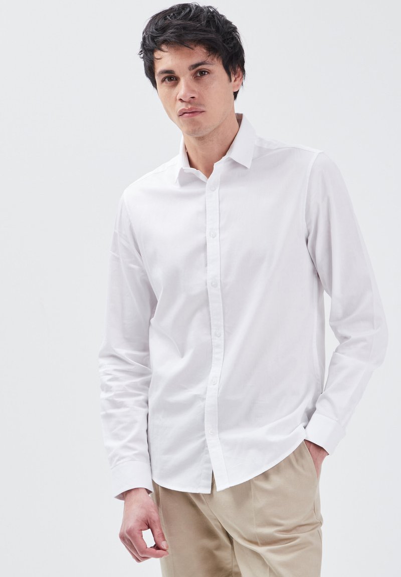 Witte lange mouwen knoopshirt van katoen. Heeft een klassieke kraag en knoopsluiting, gedragen met beige broek. Gladde textuur.