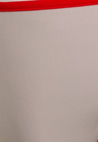 Tecido bege com uma textura suave, apresenta uma faixa elástica vermelha contrastante ao longo da borda superior, criando um design simples e aerodinâmico.