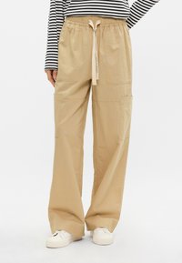 Μπεζ παντελόνι με φάρδος και ελαστική μέση με κορδόνι. Διαθέτει δύο μεγάλες πλαϊνές τσέπες και απαλό υλικό.