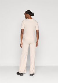 Ανοιχτό μπεζ ριμπ πλεκτό τοπ και παντελόνι με φαρδιά μπατζάκια που ταιριάζουν. Το σύνολο έχει κοντά μανίκια και άνετη εφαρμογή, συνδυασμένο με μαύρα παπούτσια.