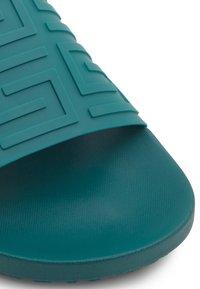 Tongs en teal avec un dessus texturé présentant un motif géométrique. Le matériau est lisse avec une finition légèrement mate. Design à bout rond.