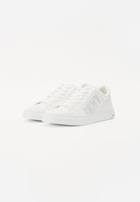 White canvas sneakers with a textured finish, featuring a logo in shiny accents, round toe, lace-up design, and flat rubber sole.