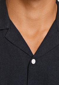 Chemise bleu marine à manches courtes en tissu texturé avec un col cranté et un seul bouton blanc au niveau du col.
