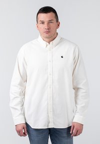 Weißes Hemd mit Knöpfen aus strukturiertem Stoff, mit Kragen, langen Ärmeln und einem kleinen schwarzen Logo auf der linken Brust.