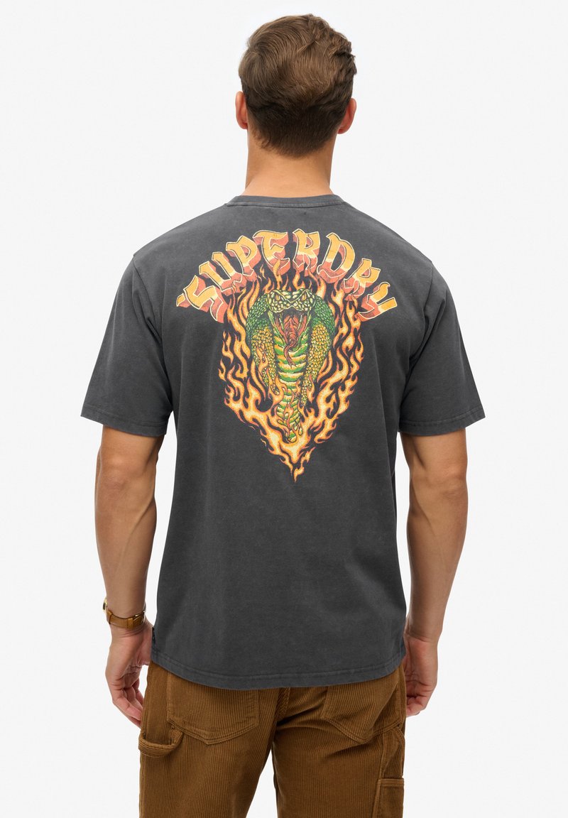 Szary bawełnowy t-shirt z wyrazistą, wielokolorową grafiką smoka otoczoną płomieniami oraz napisem "SUPERDRY" powyżej.