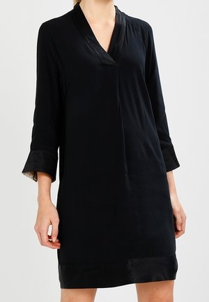 Robe noire avec un col en V et des manches trois-quarts. Fabriquée en tissu lisse avec une légère brillance. Présente une coupe simple et ample.