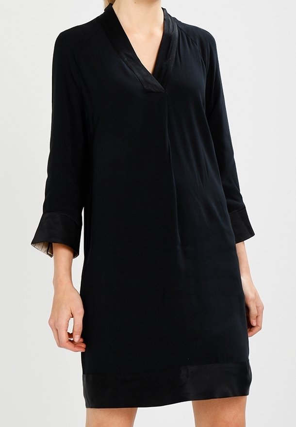 Robe noire avec un col en V et des manches trois-quarts. Fabriquée en tissu lisse avec une légère brillance. Présente une coupe simple et ample.