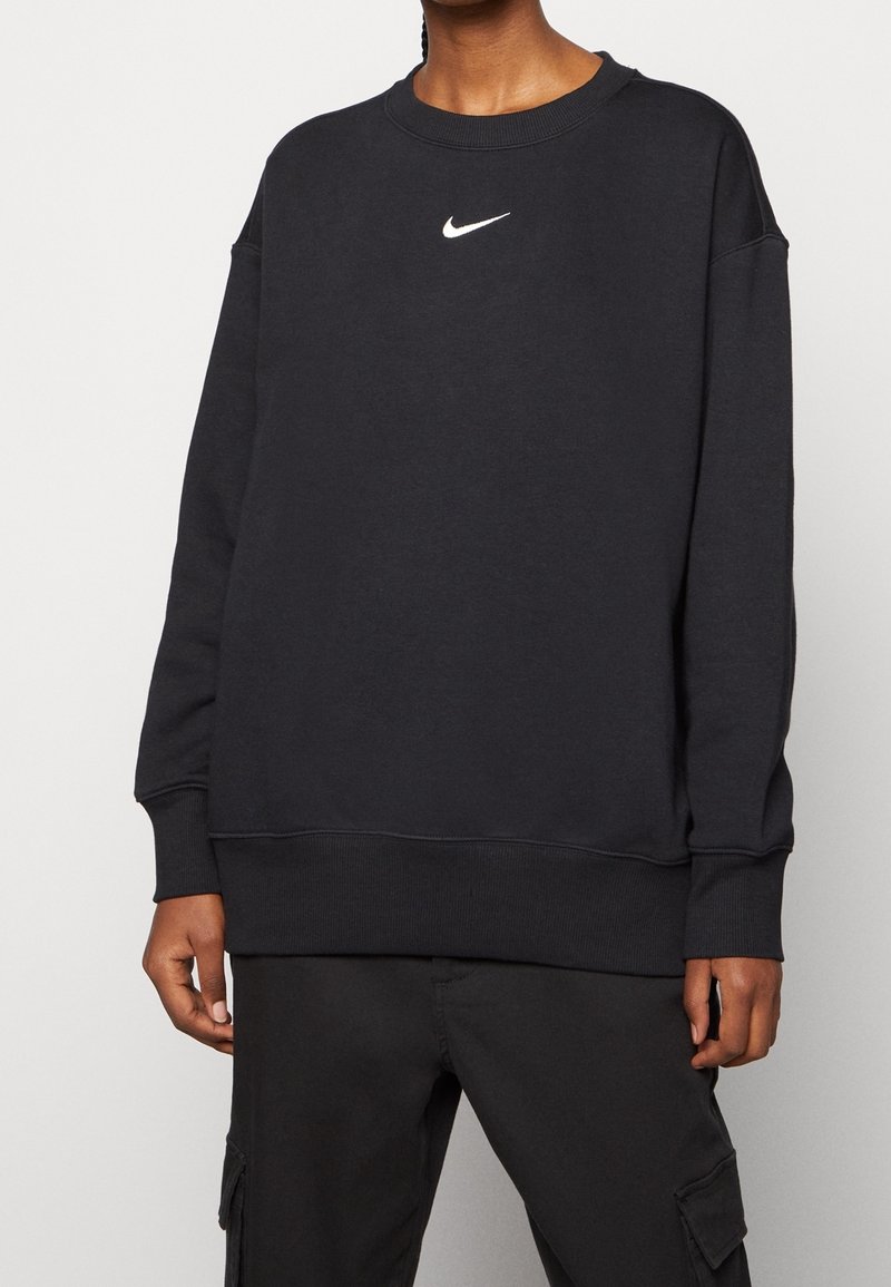 Personne portant un sweat-shirt Nike noir à manches longues avec un petit logo blanc Swoosh sur la poitrine et un pantalon cargo noir.