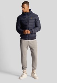 Navy puffer jacket with horizontal stitching, zip closure, and a hood. Paired with light gray joggers and white sneakers.