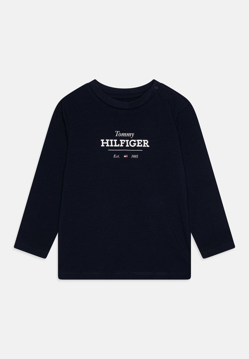 Long-sleeve navy blue cotton t-shirt with crew neck; features white "Tommy HILFIGER" logo and "Est. 1985" text. Snap button at shoulder.
