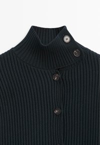 Schwarzer, gerippter Strickpullover mit hohem Umschlagkragen, der durch zwei Knöpfe gesichert ist, und einer Knopfleiste in der vorderen Mitte.