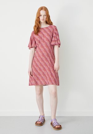 Vestido padronizado em vermelho e branco com mangas curtas e volantes, com uma bainha até ao joelho, combinado com sandálias lilás de tiras e solas de madeira.