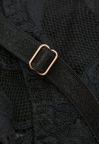 Schwarzer verstellbarer Riemen mit goldenem Metall-Schieber auf schwarzem Spitze- und Mesh-Stoff, der detaillierte Textur und Nähte zeigt.