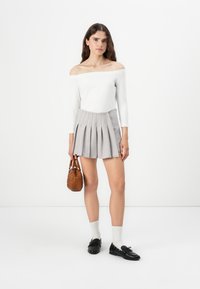 Top bianco a spalle scoperte con maniche lunghe, gonna grigia plissettata, scarpe nere e borsa intrecciata marrone. Design semplice con silhouette aderente.