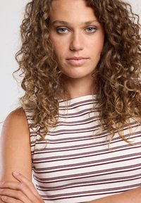 Striped sleeveless top in cream and maroon. It features a ribbed texture and a fitted design, with a high neckline and visible shoulder.