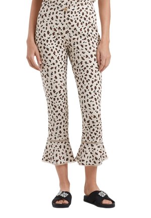 Weiße, verkürzte Hosen mit braunem und schwarzem Leopardenmuster, ausgestellte Säume mit Spitzenbesatz, getragen mit schwarzen Slide-Sandalen, die mit Strasssteinen verziert sind.