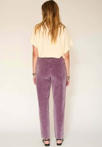 Pantalon en velours côtelé violet avec une coupe droite, cinq poches, et une taille haute, associé à un haut beige ample.