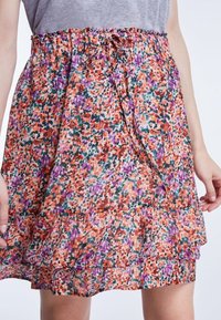 Falda de estampado floral con volantes en capas. Presenta una cinturilla con cordón, en tonos naranja, púrpura, verde y rosa sobre una tela ligera.