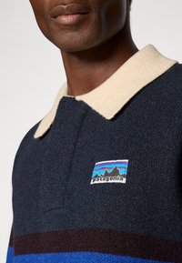 Maglione Patagonia, con un corpo in maglia blu scuro, colletto crema e motivi a righe orizzontali in blu e bordeaux. Logo sul petto.