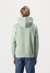 Felpa verde chiaro con un ampio cappuccio e polsini a coste. Realizzata in tessuto morbido, ha una vestibilità comoda e un orlo dritto, abbinata a jeans blu.