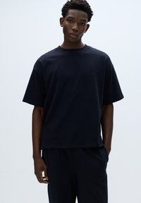 Tyrkysovo modré bavlnené tričko s vo�ľným strihom, krátkymi rukávmi, okrúhlym výstrihom a hladkou textúrou. Doplnené zhodnými tmavými nohavicami.