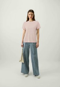 T-shirt de algodão rosa claro com decote redondo, combinado com calças de ganga de perna larga e uma pequena bolsa prateada. Textura suave, ajuste descontraído.