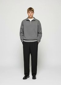 Grauer Sweatshirt mit Reißverschluss und hohem Kragen, kombiniert mit schwarzer Hose und schwarzen Schuhen. Einfaches Design, minimale Akzente und glatte Textur.