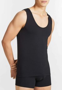 Top in cotone nero senza maniche con scollatura arrotondata e fori per le braccia, caratterizzato da un design aderente e da una texture liscia. Abbinato a pantaloni corti neri coordinati.