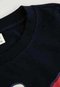 Granatowa bawełniana koszulka z okrągłym dekoltem, o gładkiej teksturze i subtelnych detalach nadruku w okolicy kołnierza. Widoczna metka wewnątrz.