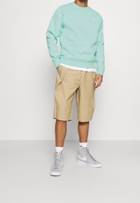 Felpa azzurra chiara, pantaloni corti khaki e sneakers grigie. Design aderente, polsini a costine e cuciture dettagliate sui capi.