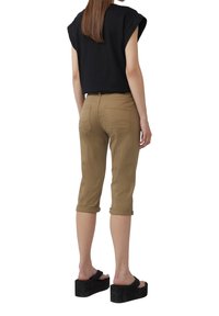 Czarny top z krótkim rękawem, khaki spodenki 7/8 z podwiniętymi mankietami i czarne sandały na platformie. Wyraźne przeszycia na kieszeniach. Gładkie faktury.