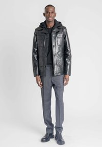 Zwarte leren jas met voorzakken en een capuchon, gecombineerd met grijze nette broek en zwarte enkellaarzen. Eenvoudig, gestructureerd ontwerp.