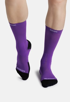 Legs wearing mid-calf purple socks with black heels and toes, showing ribbed texture and white "XX SOCKS" branding near toes.
