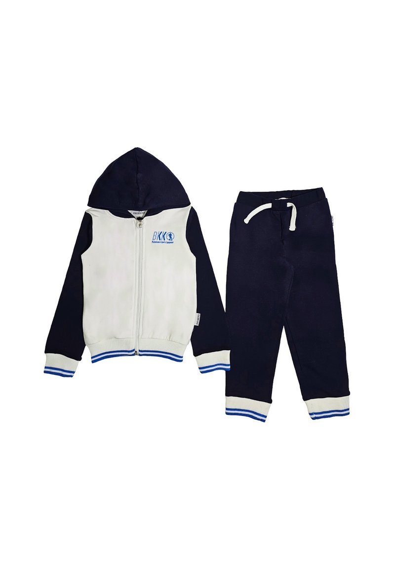 Giacca con cappuccio con davanti bianco e maniche blu scuro, con accenti blu e un logo. Abbinata a pantaloni blu scuro, entrambi realizzati in tessuto morbido.