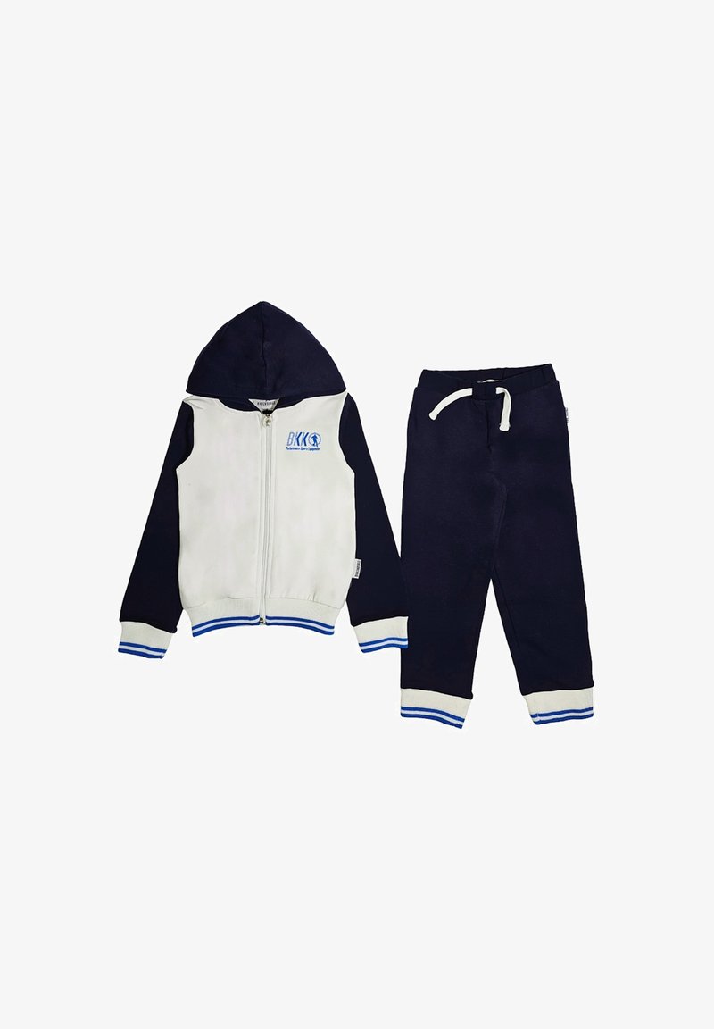 Giacca con cappuccio con davanti bianco e maniche blu scuro, con accenti blu e un logo. Abbinata a pantaloni blu scuro, entrambi realizzati in tessuto morbido.