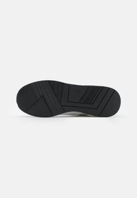 Suela de zapatilla de goma negra con un patrón texturizado que presenta surcos y crestas para mejorar la tracción. Logotipo grabado en el lateral.