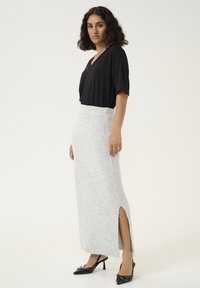 Un haut noir à col en V associé à une jupe maxi en tricot côtelé grise avec une fente sur le côté. Des mules à talons noirs complètent l'ensemble.