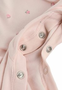 Gros plan sur un tissu rose avec de petits imprimés fleuris et des boutons-pression argentés le long des bords cousus.