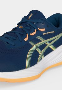 Μπλε αθλητικό παπούτσι Asics Gel-Cumulus με κίτρινες και πράσινες ρίγες, σκούρα μπλε κορδόνια και πορτοκαλί λεπτομέρειες σε λευκή και πορτοκαλί σόλα.