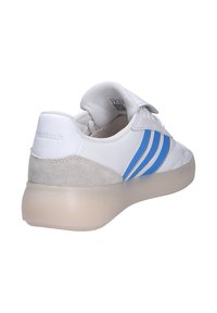 Baskets blanches basses avec des rayures bleues, un patch de talon en daim beige, un col rembourré et une semelle translucide vues de l'arrière en angle vers la droite.