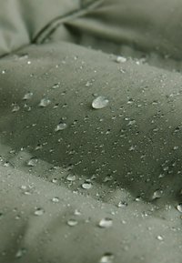 Vandafvisende grønne stof med en tekstureret overflade, der har vanddråber på materialet, hvilket fremhæver dets vandtætte egenskaber.