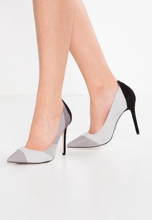 Szare i czarne zamszowe szpilki z wydłużonym noskiem oraz geometrycznym wzorem w kolorowe bloki, z cienkim obcasem typu stiletto.