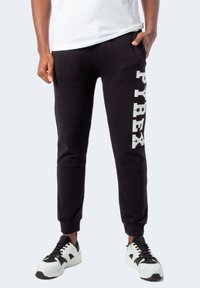 Pantaloni tuta neri con la scritta "PYREX" stampata in bianco sulla gamba sinistra, vita elastica e gambe affusolate. Abbinati a sneakers bianche e nere.