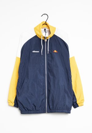 Cazadora cortavientos a bloques de color, con cuerpo azul marino, mangas y capucha amarillas, hombros blancos, cremallera frontal y logo de ellesse en el pecho, colgada en una percha.