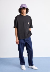 Black oversized cotton t-shirt with a chest pocket, paired with dark blue jeans and white sneakers, topped with a light purple cap.