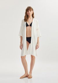 Hvid kimono-lignende cover-up lavet af letvægtsstof, med korte ærmer, løst fit og blonde detaljer på ærmerne.