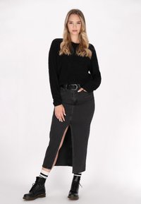 Schwarzer, flauschiger Pullover, kombiniert mit einem schwarzen Denim-Rock mit hohen Schlitzen. Das Model trägt schwarze Schnürstiefel und kniehohe gestreifte Socken.