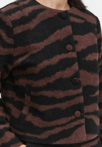 Wool blend jacket in black with dark brown zebra stripes, featuring a round neckline and two front buttons. Textured fabric with a cropped design.
