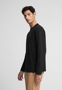 Czarna koszulka z długim rękawem z bawełny, z okrągłym dekoltem, subtelnym logo i prostym wykończeniem u dołu. Gładka faktura.