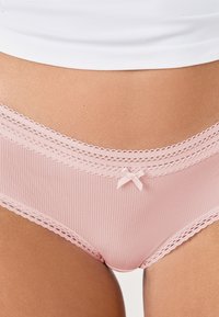 Mutandine rosa chiaro a coste con pizzo, caratterizzate da un piccolo dettaglio a forma di fiocco al centro e una texture morbida e liscia.